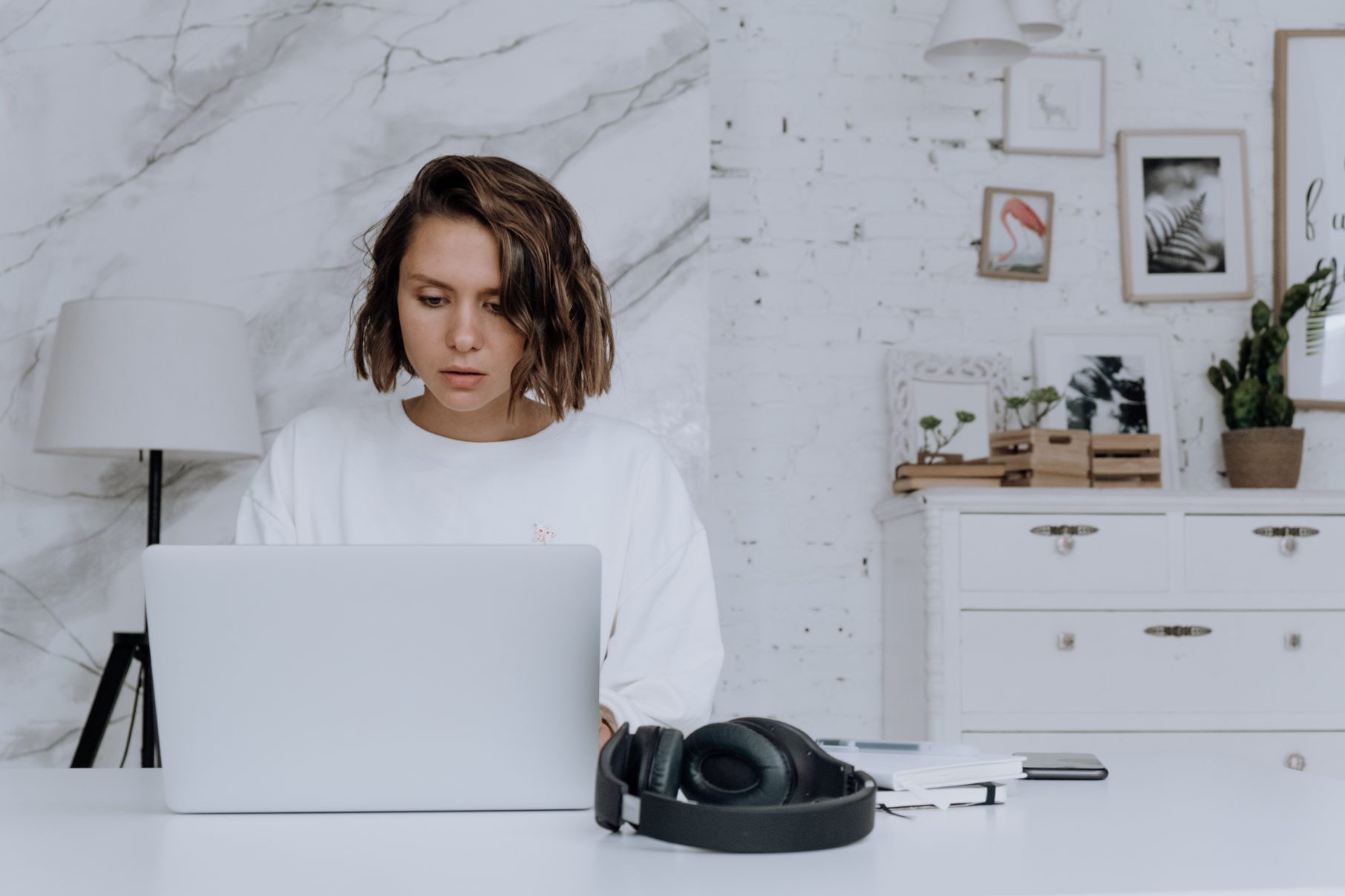 woman in white room using laptop with headphones on desk holiday marketing ideas